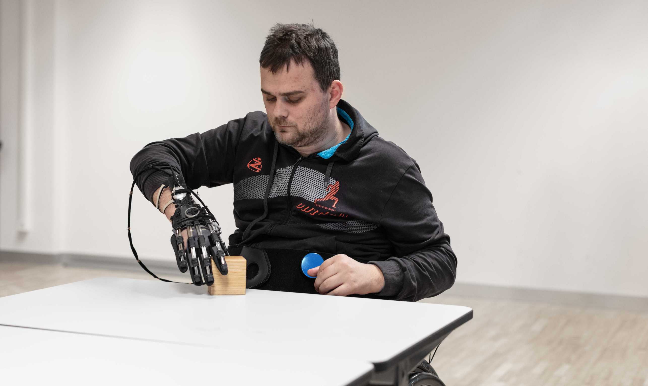 Person with limited function of the right hand lifts a wooden cube with the help of a hand exoskeleton